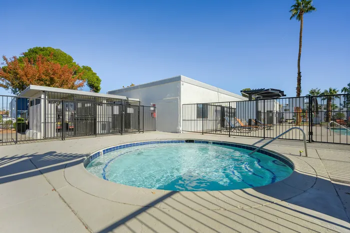 Inviting apartment complex with a sparkling spa in a sunny, private fenced area and lush greenery, perfect for relaxation.