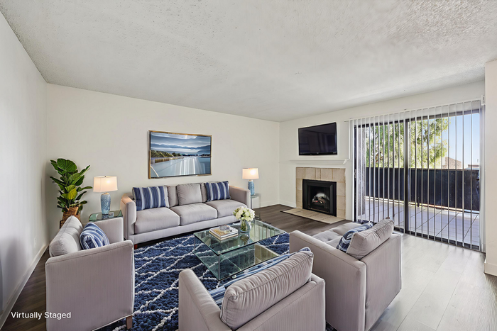 Bright and inviting living room with modern decor, plush gray sofas, and a cozy fireplace, enhanced by natural light through large sliding glass doors.
