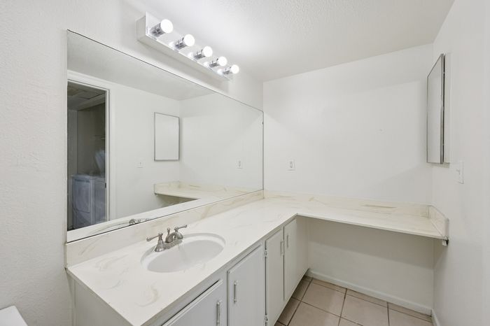 Elegant bathroom with pristine white vanity, expansive mirror, and chic lighting, offering a refreshing and modern atmosphere.