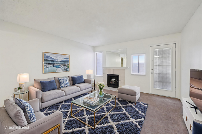 Elegant living room with modern gray sofas, a cozy fireplace, and vibrant blue decor, featuring natural light and contemporary furnishings.
