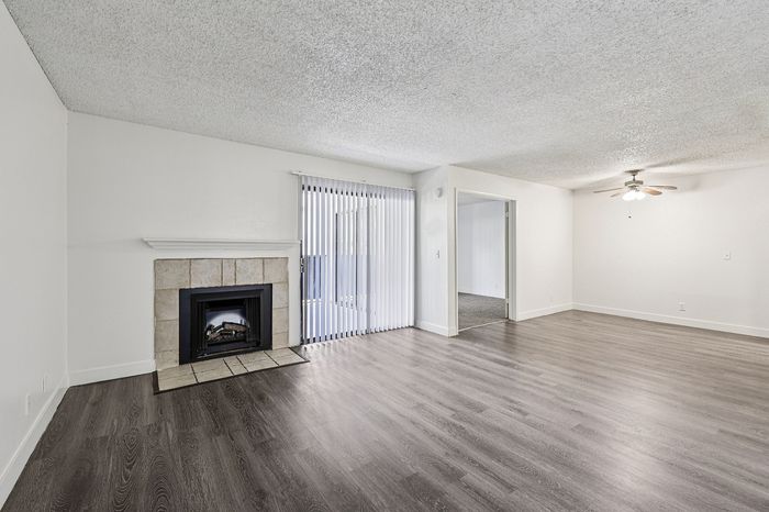 Bright and spacious living room with elegant wooden flooring, cozy fireplace, ceiling fan, and large sliding glass door leading to a private balcony, perfect for modern living.