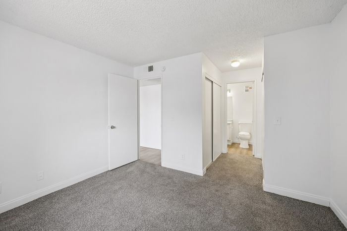 Bright and inviting bedroom with plush carpet, contemporary white walls, and convenient ensuite bathroom access.