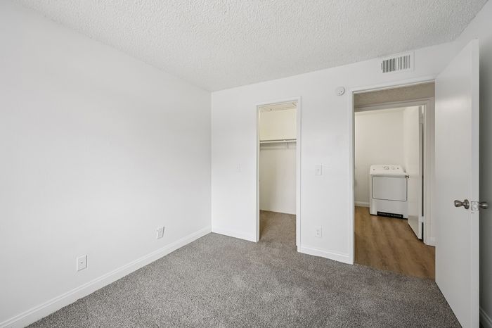 Bright and inviting bedroom with plush carpet, featuring a spacious walk-in closet and convenient in-unit laundry space.