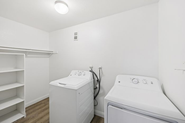 Chic and modern laundry room featuring sleek white washer and dryer units, enhanced by elegant shelving and warm wood flooring.