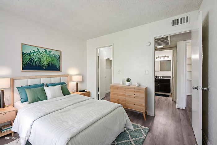 Beautifully staged bedroom featuring a plush bed with green accents, modern wooden furniture, and an inviting ambiance. Adjoining bathroom adds convenience and luxury.