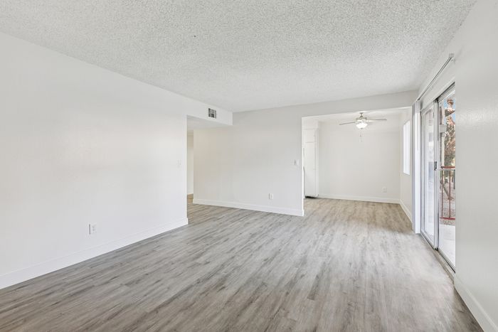 Spacious modern living area with sleek wood flooring, abundant natural light through large sliding glass doors, and a ceiling fan for enhanced comfort.