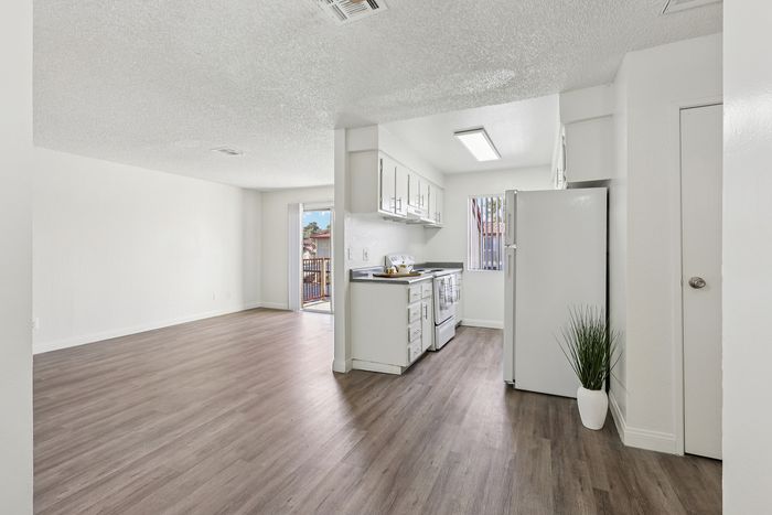 Bright, open-concept kitchen and living area with sleek hardwood flooring and modern white cabinetry, leading to a sunny balcony.