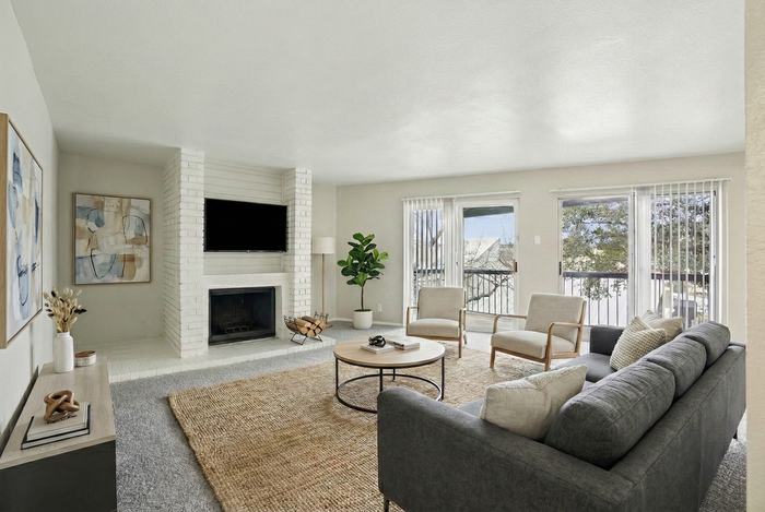 Bright and inviting living room with a large window view, featuring a cozy fireplace, elegant gray sofa, and modern armchairs, perfect for relaxation and entertaining.