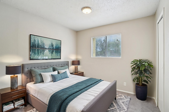 Modern and inviting bedroom with plush bedding, elegant decor, and ample natural light from a large window. Features stylish artwork and contemporary furnishings in a virtually staged setup.