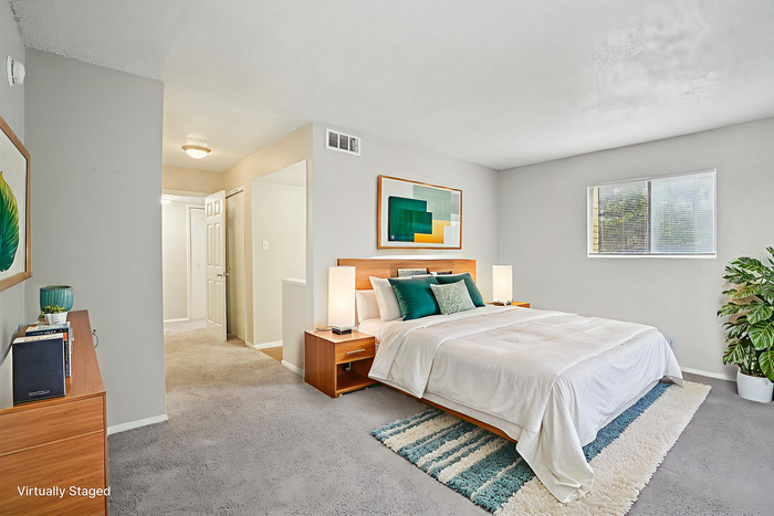 Brightly lit bedroom with modern decor, plush carpeting, and inviting king-size bed, accentuated by a stylish rug and large window for ample natural light.
