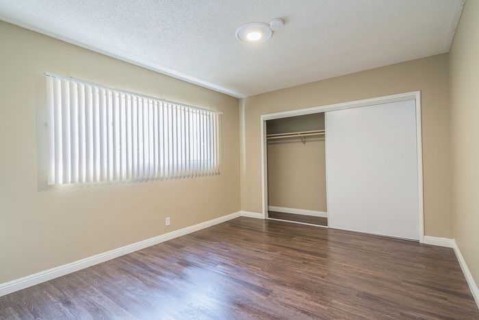 Bright, modern bedroom with laminate flooring, large window with vertical blinds, and a spacious closet.