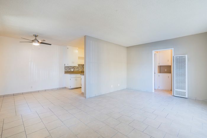 Bright living area with modern ceiling fan, adjacent to a sleek kitchen featuring tiled backsplash and neutral tiled flooring.