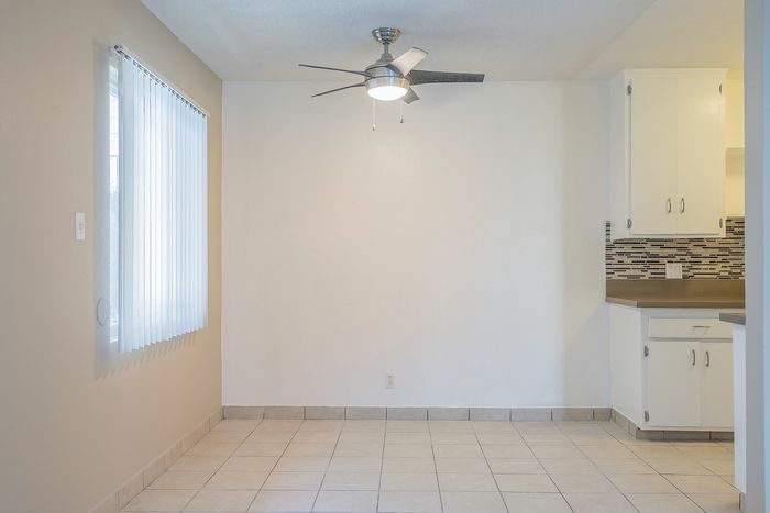 Inviting space with sleek tiled flooring, modern ceiling fan, and adjacent kitchen featuring elegant cabinetry and backsplash.