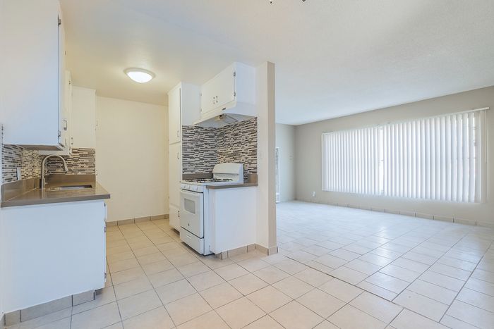 Bright open-plan living space with a modern kitchen featuring sleek white cabinets, a stylish backsplash, and abundant natural light.