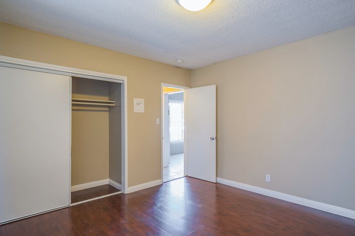 Bright and inviting bedroom with sleek hardwood floors, spacious closet, and warm neutral walls, perfect for a cozy retreat.
