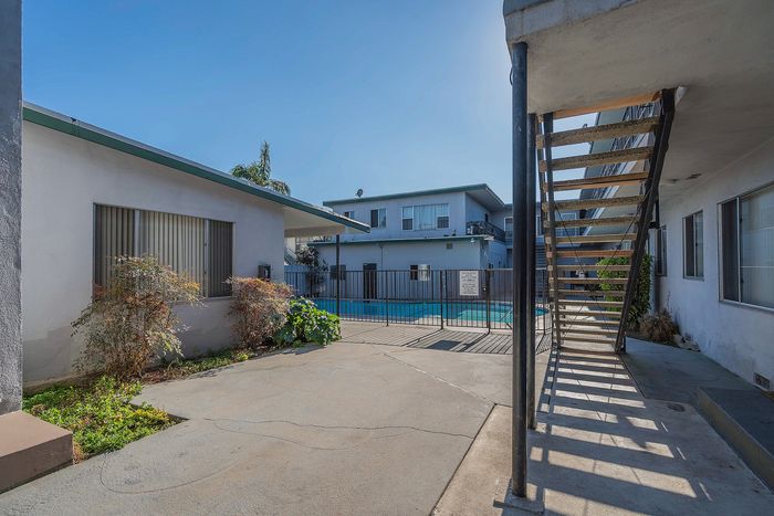 Inviting courtyard with vibrant greenery and gated pool access, nestled between two charming apartment buildings.