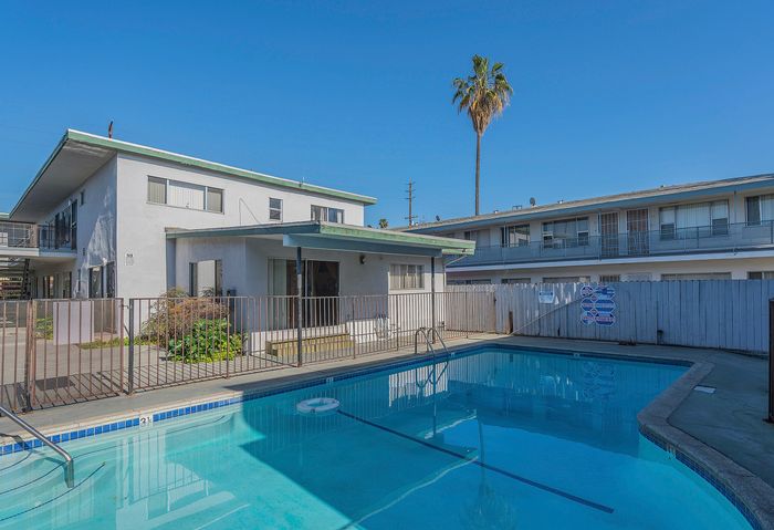 Sunny apartment complex featuring a refreshing swimming pool and modern architecture, perfect for relaxed living.