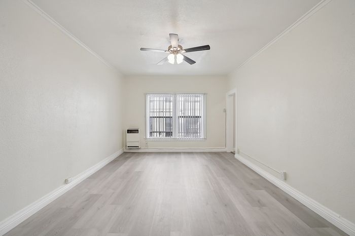 Bright and airy living room with modern ceiling fan and large window, featuring elegant light wood flooring and neutral walls for a spacious feel.
