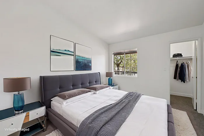 Virtually staged serene bedroom with stylish gray bed, chic side tables, and soft lighting; features a spacious closet and beautiful window view.