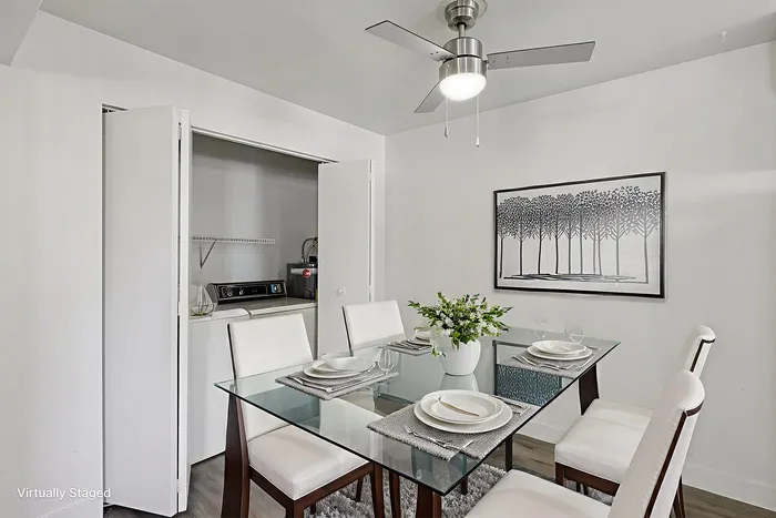 Chic dining area with elegant glass table set for four, modern art on the wall, and a convenient in-unit laundry nook.