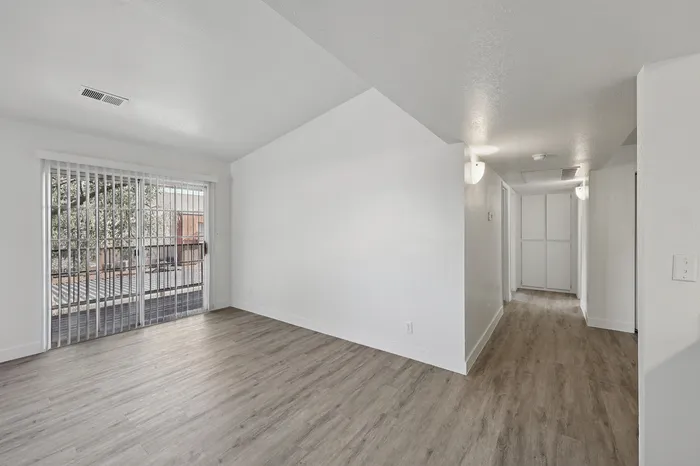 Bright and airy living space with modern wood flooring, large glass doors leading to a balcony, and a welcoming hallway.