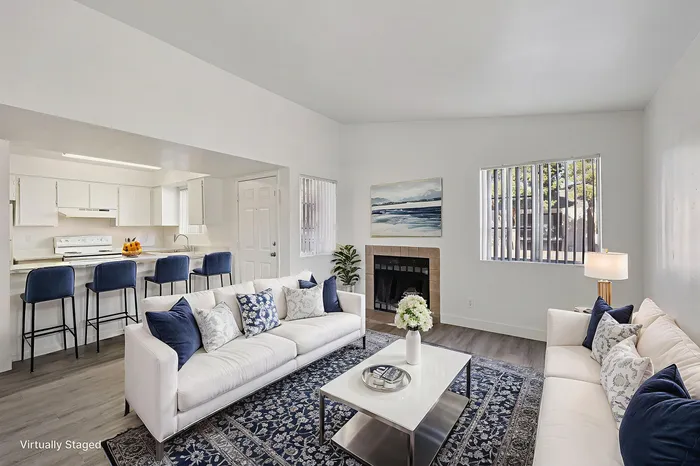 Modern open-concept living room with cozy fireplace, elegant white sofas, and stylish kitchen with bar seating, accented by tasteful decor.