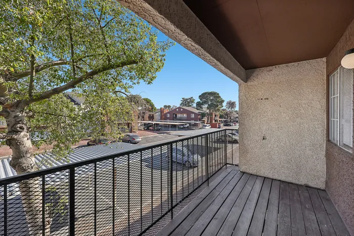Charming apartment balcony with a wooden deck, overlooking a serene neighborhood with lush trees and parked cars.