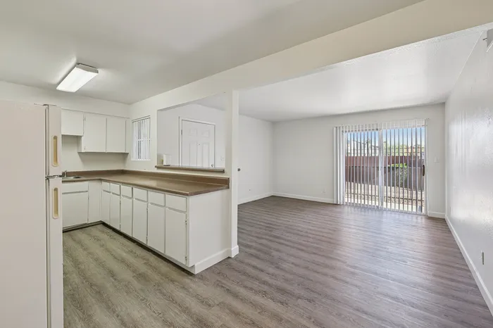 Inviting open-plan apartment with sleek flooring, bright kitchen, and large sliding doors to a sunlit patio.
