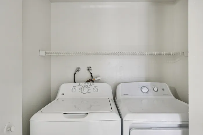 Modern apartment laundry area featuring a sleek washer and dryer set with an overhead storage shelf.