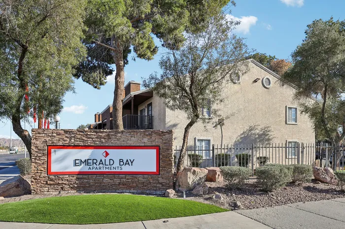 Inviting entrance to Emerald Bay Apartments framed by lush greenery and elegant stone sign, showcasing a serene and welcoming residential community.