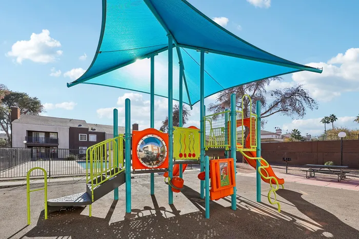 Vibrant playground area with colorful slides and climbing structures, shaded by a stylish canopy, offering a fun and inviting space for children.