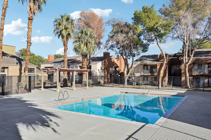 Charming apartment complex featuring a sparkling blue swimming pool surrounded by lush palm trees and cozy residences.