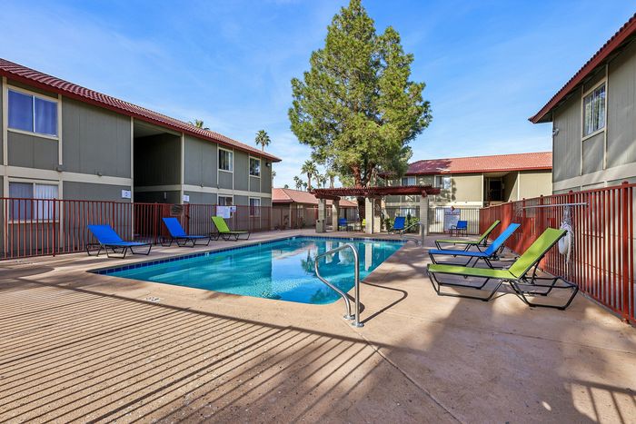 Inviting apartment complex with a sparkling outdoor swimming pool, surrounded by lounge chairs and lush greenery, perfect for relaxation and entertainment.