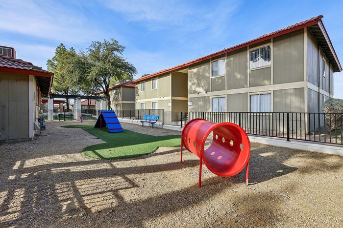 Inviting apartment exterior with a vibrant children's play area, featuring a colorful slide and tunnel set against a backdrop of manicured greenery and modern architecture.