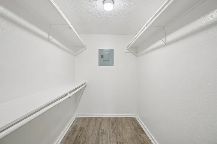 Spacious walk-in closet with sleek white shelving and elegant wooden flooring, perfect for organized living.
