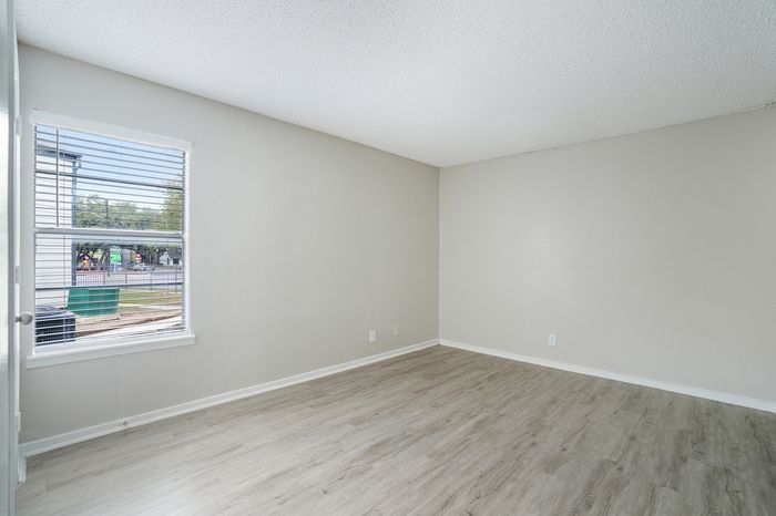 Bright empty room with large window, light wood flooring, and neutral walls offering a versatile space to personalize.