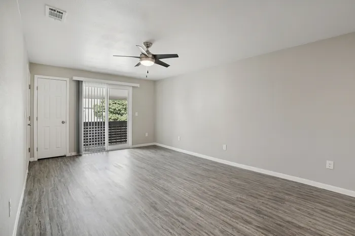 Bright, modern living space with sleek hardwood floors, sliding patio doors, and ceiling fan, perfect for comfortable living and entertaining.