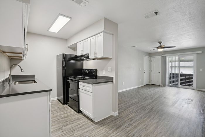 Bright open-plan kitchen and living area with sleek black appliances, elegant countertops, and stylish ceiling fan. Perfect for modern living.