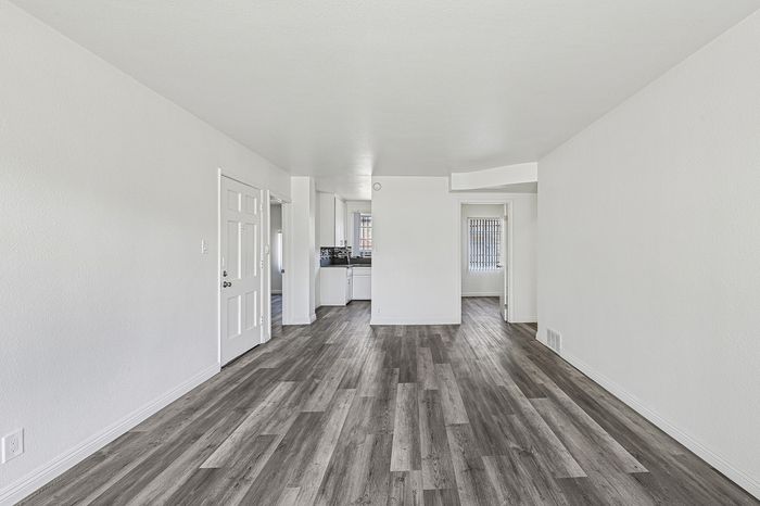 Bright and airy open-concept living space with modern gray flooring and sleek white walls, leading into a cozy kitchen area.