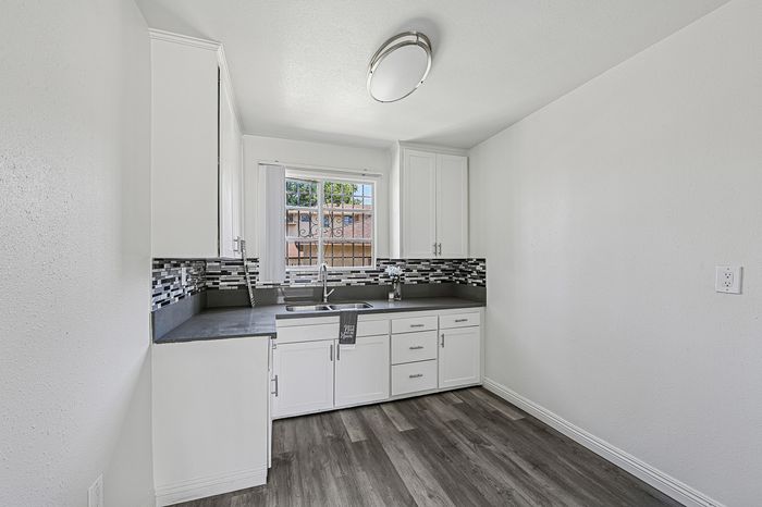 Chic modern kitchen with sleek white cabinetry, elegant dark countertops, and a stylish backsplash, offering a bright and refreshing atmosphere.
