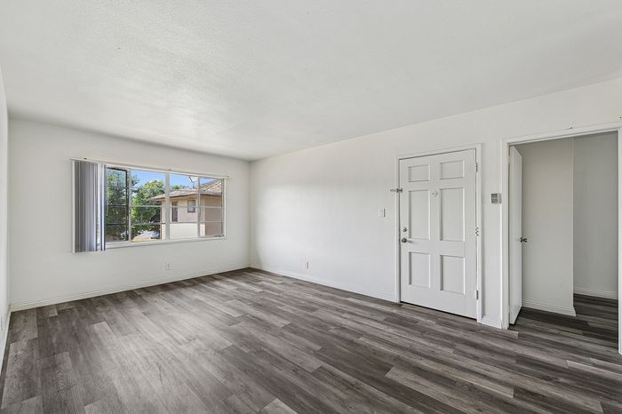 Bright and spacious empty room with elegant wood-style flooring, large window, and neutral white walls.