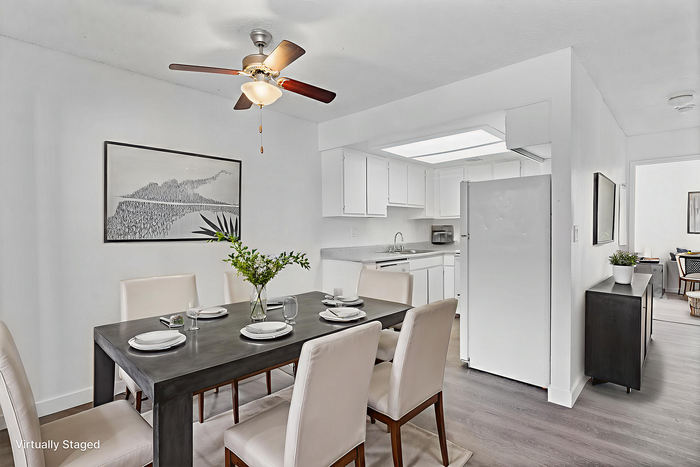 Elegantly staged dining area with a modern table set for four, adjacent to a sleek white kitchen, perfect for hosting intimate gatherings.