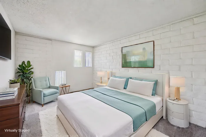 Elegant bedroom featuring a plush bed with teal accents, modern artwork, and natural light from vertical windows for a serene ambiance.