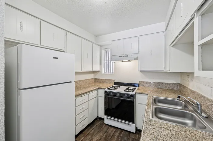 Charming kitchen featuring white cabinetry, sleek granite countertops, and modern appliances including a spacious fridge and gas stove.