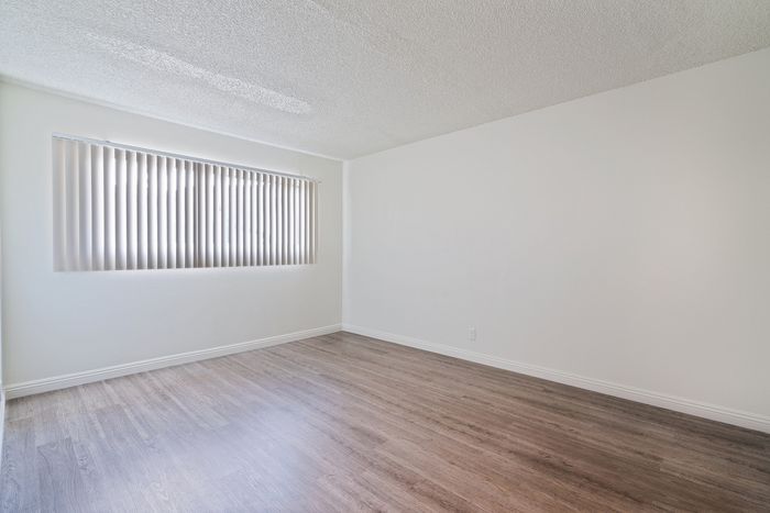 Bright, inviting room with elegant wood floors and large window blinds, perfect for customization.