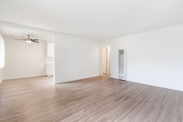 Bright and airy living space with sleek wood flooring, an elegant ceiling fan, and ample natural light flowing into the open kitchen area.