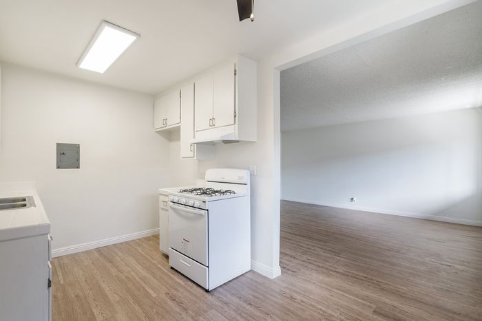 Inviting kitchen space with sleek white cabinets, modern gas stove, and elegant wooden flooring opening into a spacious living area.