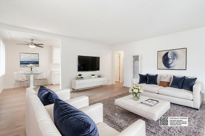 Bright and airy living room with elegant white sofas, plush blue accents, and modern art, leading to a cozy dining area.