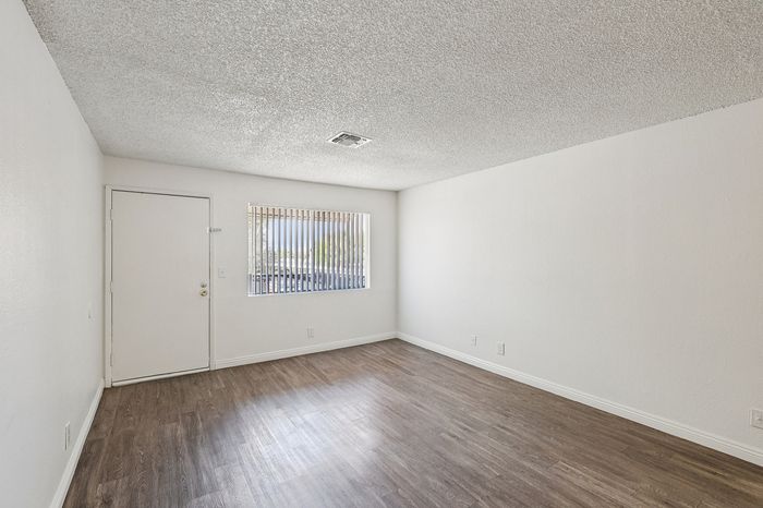 Bright and airy room with elegant wood flooring, modern white walls, and ample natural light from a large window.