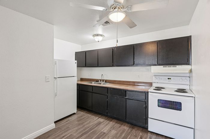 Modern kitchen with sleek dark cabinets, white appliances, and stylish wooden flooring.